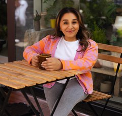 Shani Dhanda sitting at table with drink, outside